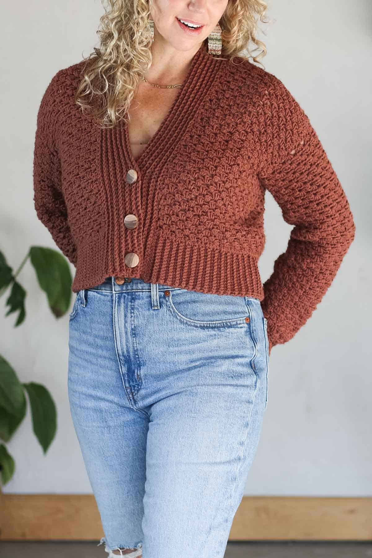 Close-up of a rust-colored half double crochet cardigan with wooden buttons, worn by Jess Coppom.