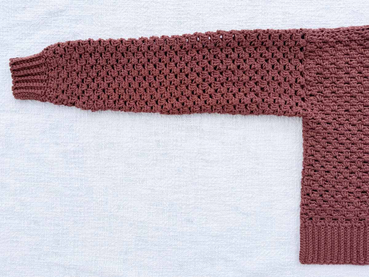 Flat lay of the cardigan body panel corner showing the ribbed hem and half double crochet stitch pattern in Lion Brand Color Theory yarn.
