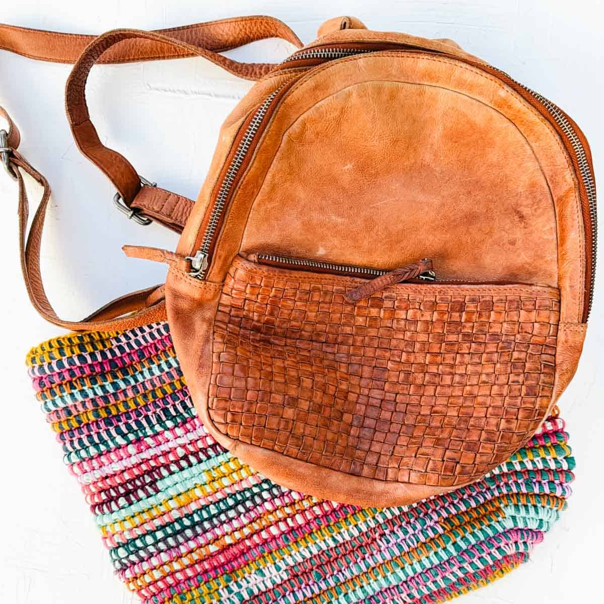 Leather backpack with a broken zipper on top of a crocheted bag.