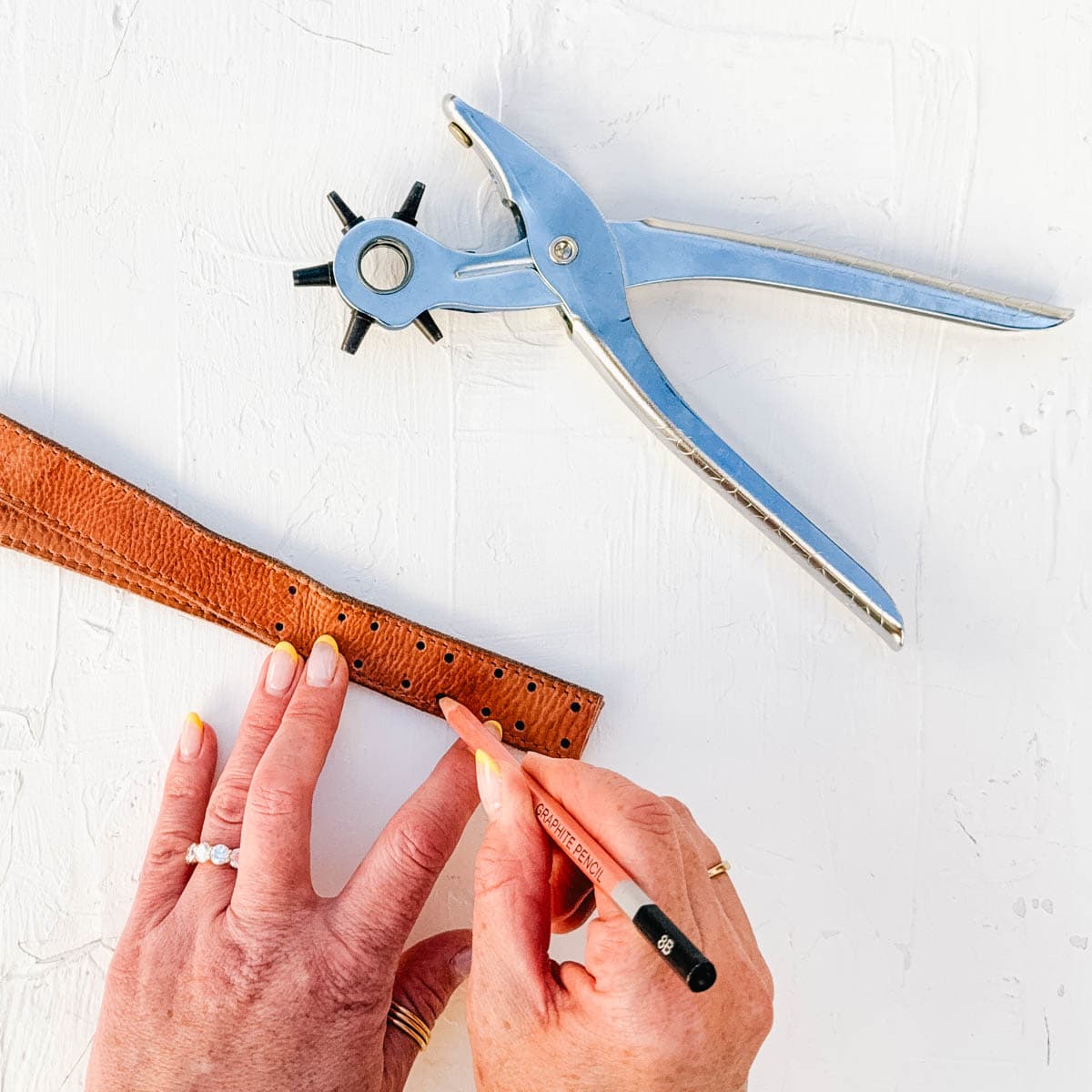 Hands demonstrating marking hole placement on a leather strap.
