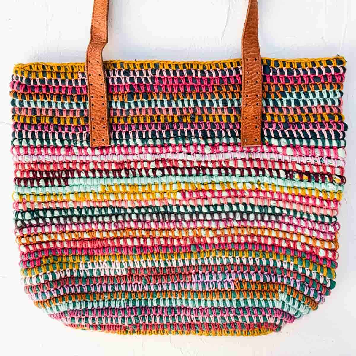 Striped, scrappy crochet bag with leather straps placed on top in preparation for sewing them on.