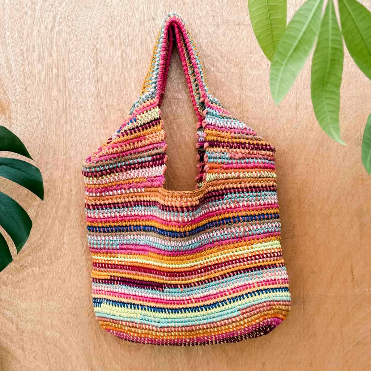 A scrap yarn crochet bag hanging against a wooden wall.