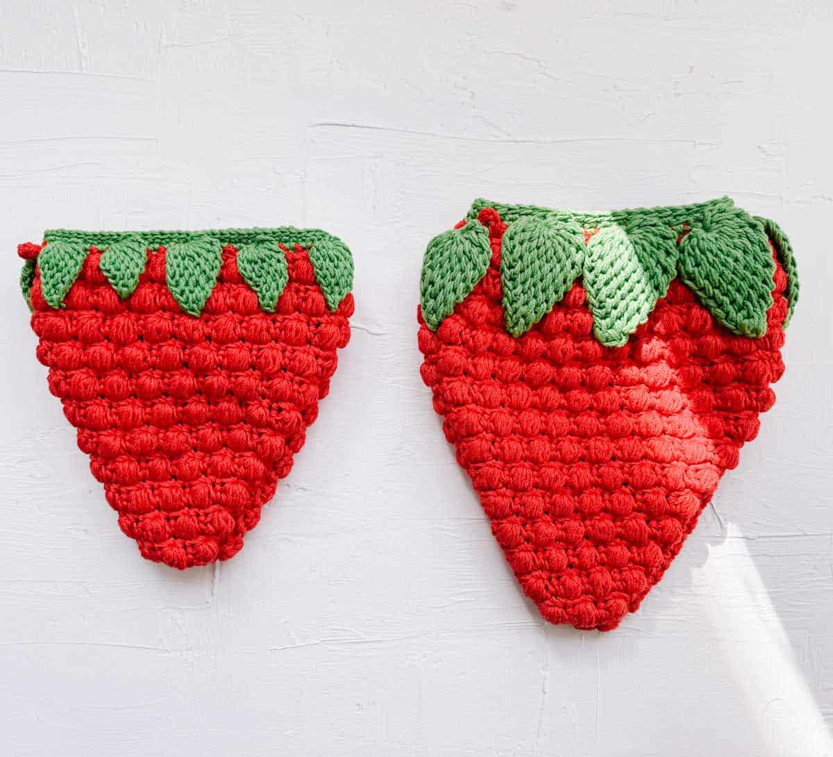A small crochet strawberry purse next to a larger strawberry bag.