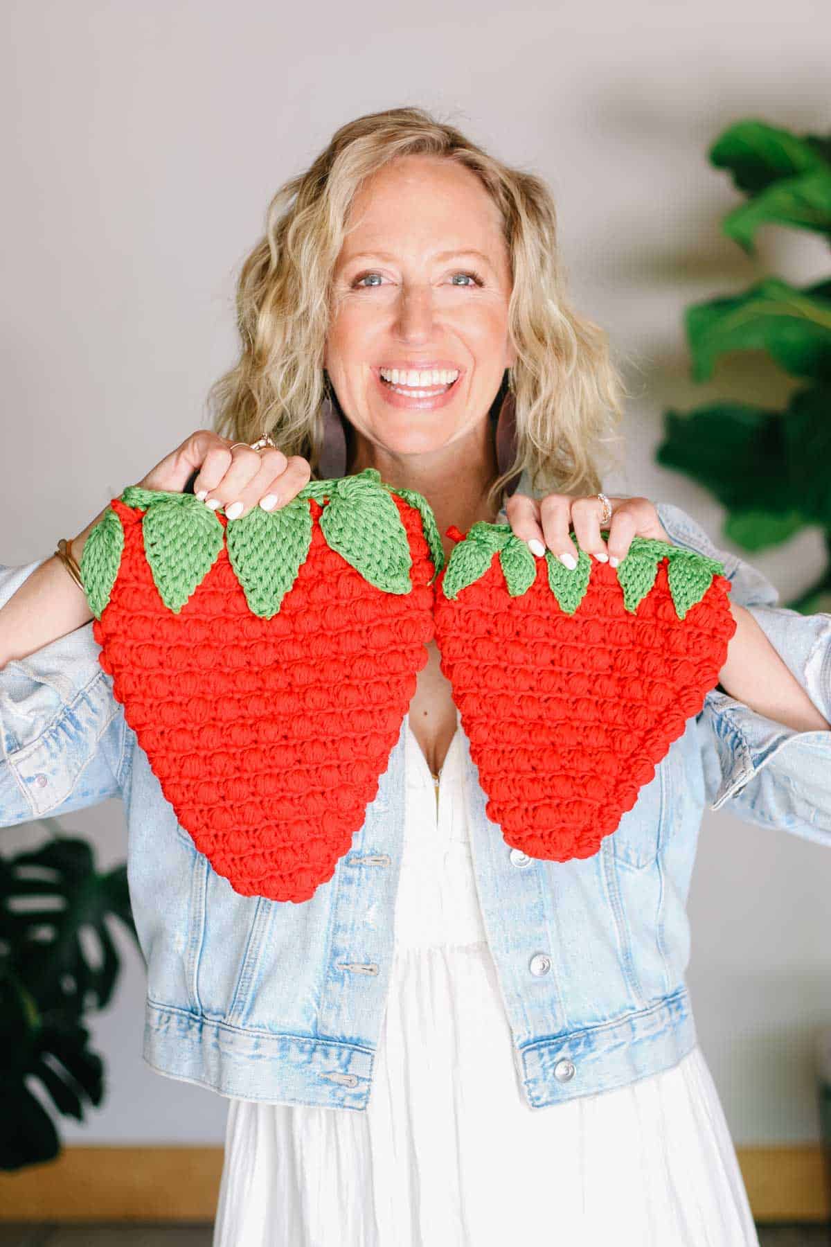 Two crocheted strawberry bags held by crochet designer Jess Coppom of Make & Do Crew.