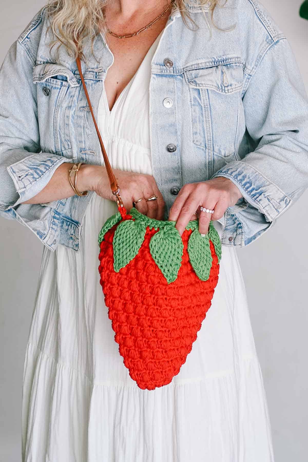 Crochet strawberry bag with a leather strap.