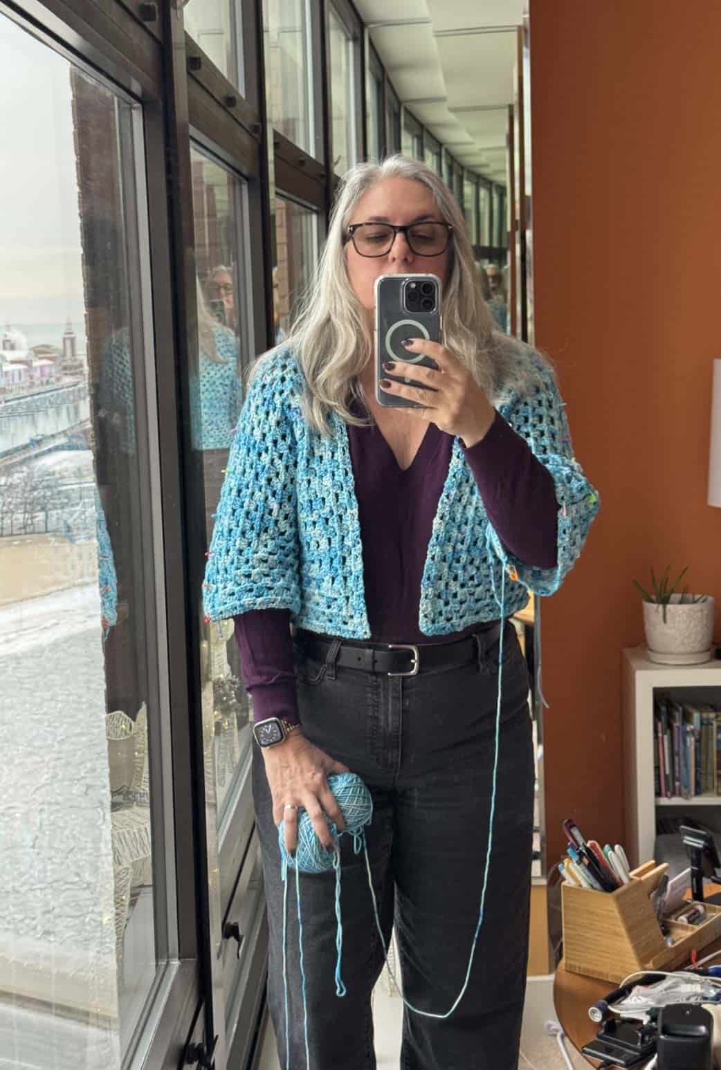 Woman wearing an in-progress crochet sweater taking a selfie.