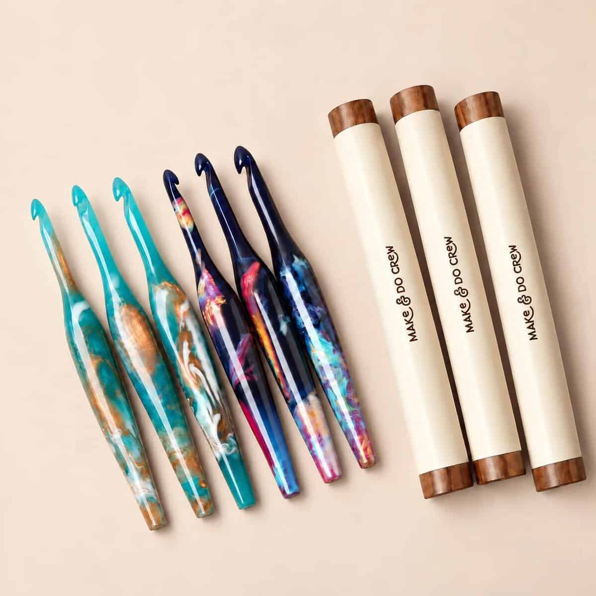 Make & Do Crew ergonomic resin crochet hooks in teal and navy swirls, beside their storage tubes